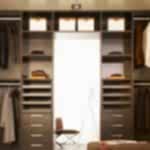 A well-organized walk-in wardrobe with dark wooden shelves, drawers, and hanging rods. Various clothing items such as suits, shirts, and jackets are neatly arranged. In the back, a chair and a light stand are visible through an opening, enhancing the space's modern feel and epitomizing the perfect walk-in-wardrobe project.