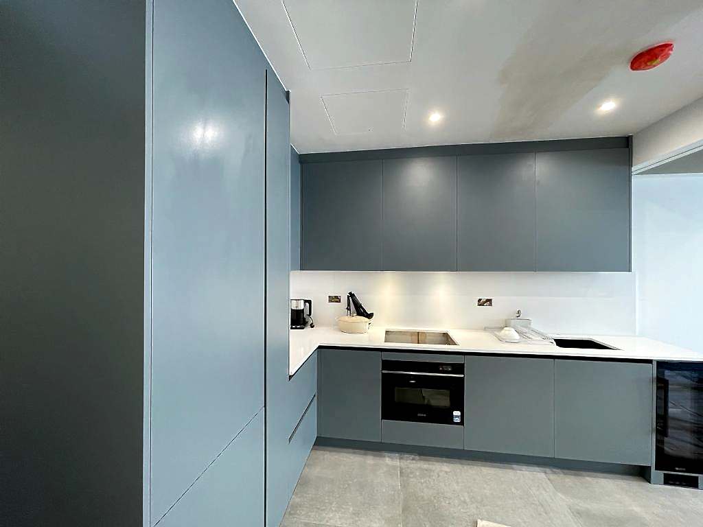 A modern kitchen with grey cabinets, white countertops, and a sleek built-in oven. The kitchen also features an electric cooktop, a microwave, a small appliance on the counter, and recessed lighting on the ceiling, complementing the elegance of fitted furniture throughout the space.